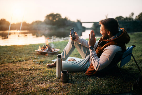 Happy man has video call over smart phone while camping by lake.