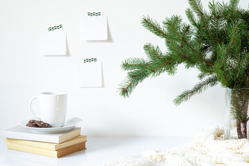 Obraz na płótnie Canvas Festive breakfast still life.Cup of coffee with cookies, books and vase with fir branch.Empty notepads mockup hanging on the wall.Christmas decor.Working space, home office.Happy new year resolution