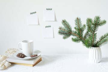 Festive breakfast still life.Cup of coffee with cookies, books and vase with fir branch.Empty notepads mockup hanging on the wall.Christmas decor.Working space, home office.Happy new year resolutions