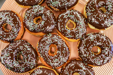 Chocolate filled donuts in a brown platter and on top of it small, colorful candy confetti
