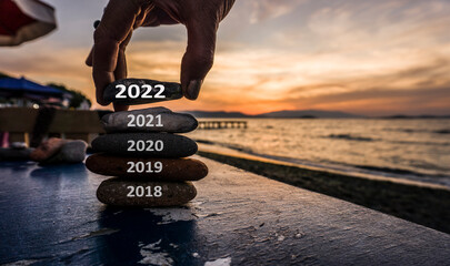 Happy new year 2022 is coming, man adding stone to pebble tower because new year 2022 replace 2021....