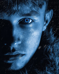 Portrait of a guy with fur around his neck and blue eyes on a black background with snow