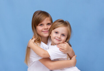 Close-up portrait of two nice cute lovely sweet attractive adorable cheerful cheery sisters wearing casual white t-shirt isolated over blue pastel background
