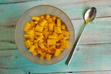 chia pudding with coconut milk and mango in a pink glass glass stands next to a spoon on a blue wooden table. top view. light dessert gluten-free, lactose-free