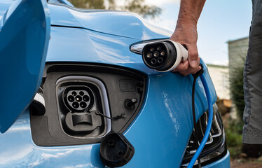 Close up view of front end of a blue electric E car showing type 2 charge plug and socket and granny cable