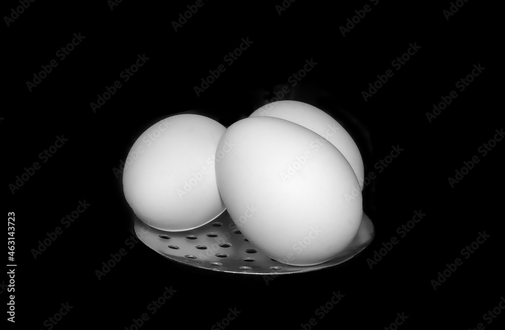 Wall mural Closeup shot of fresh eggs on a metal surface isolated on dark background