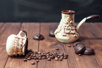 Coffee beans sprinkled from an inverted cup on a wooden surface next to chocolates