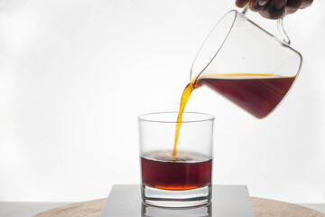 Coffee being poured into clear tumbler against bright backlight