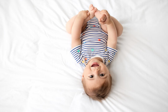 Top view of cute baby lying on white bed holding his feet
