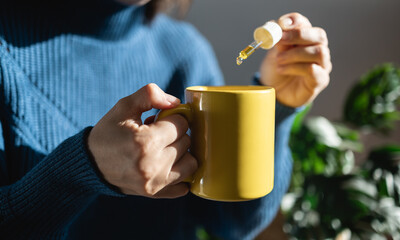 Cbd hemp oil - Woman taking cannabis oil in tea cup - Focus on left hand