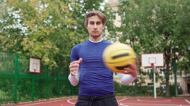 Portrait of teenage boy doing basketball drill exercise on outdoor college court. Handsome young man, college or high school student with ball and in sportswear looking at camera while practicing bask