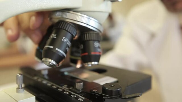 Cientista trabalhando com microsc&oacute;pio em laborat&oacute;rio, close-up. Conceito de ci&ecirc;ncia, qu&iacute;mica, biologia, medicina e pessoas, m&atilde;os analisando abjeto no microsc&oacute;pio