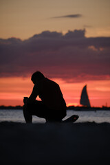 Junger Mann und Segelboot im Sonnenuntergang am Strand von Fort Myers Beach in Florida (Hochformat)