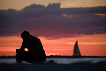 Junger Mann und Segelboot im Sonnenuntergang am Strand von Fort Myers Beach in Florida (Querformat)