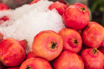 Pomegranates lying on a market stall. Red pomegranate fruits and ice to keep them fresh.