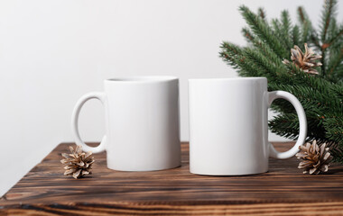 Christmas mockup two white empty tea mug on a brown wooden table and branches of a Christmas tree wreath.