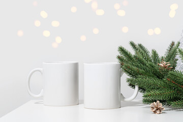 Christmas mockup white empty tea mugs on a white table and branches of a Christmas tree wreath.