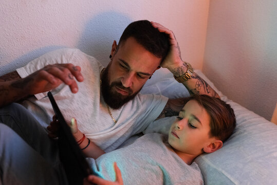 Father and son using tablet on bed