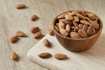 Tasty almond nuts in bowl on a wooden cutting board on wooden table, side view. Space for text