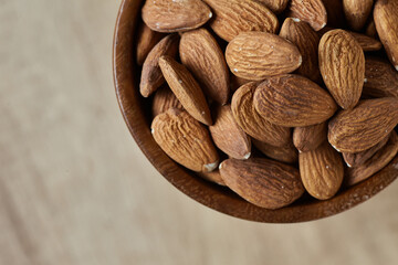 Tasty almond nuts in a bowl on a wooden table, top view. Space for text
