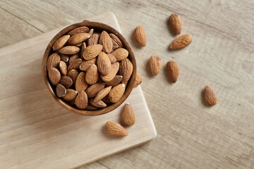 Tasty almond nuts in a bowl on a wooden table, top view. Space for text