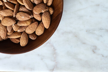 Tasty almond nuts in a wooden bowl on a marble table, top view. Space for text