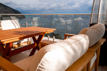 Restaurant with sea view. You can see rocks in the sea. Wooden tables and chairs with white cushions. Overcast, cloudy weather.
