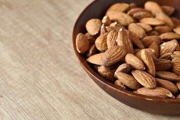 Tasty almond nuts in a wooden bowl on a wooden table, side view. Space for text