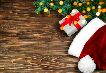 Obraz na płótnie Canvas Christmas background santa hat, fir branches, bokeh, gift box on wooden background.