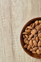 Tasty almond nuts in a wooden bowl on a wooden table, top view. Space for text