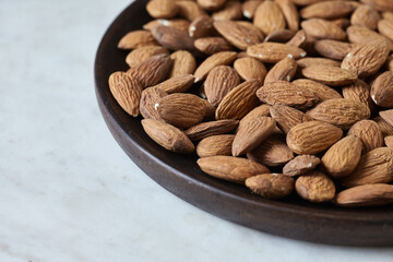 Tasty almond nuts on a wooden plate on a marble table, side view. Space for text