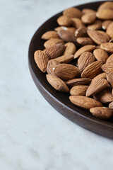 Tasty almond nuts on a wooden plate on a marble table, side view. Space for text