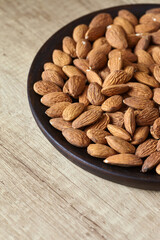 Tasty almond nuts on a wooden plate on a wooden table, side view. Space for text