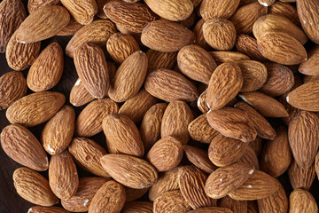 Tasty almond nuts on a wooden plate on a wooden table, top view. Space for text