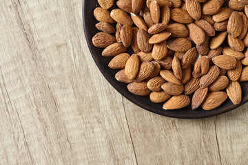 Tasty almond nuts on a wooden plate on a wooden table, top view. Space for text