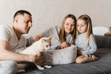 Portrait of loving family with newborn son and infant daughter. Happy caucasian family of four people. Family in the living room laying on the sofa with a cat and newborn baby. Selective focus. Film