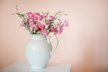 Bouquet with eustoma, summer flowers in a white vase, on a pink-beige background.