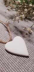 White pendant in the shape of a heart. White heart decoration. Love background. Delicate composition with a heart and flowers.