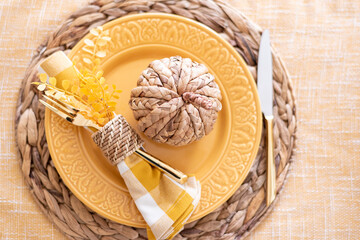 Top view of a fall table setting with yellow plate and wicker pumpkin