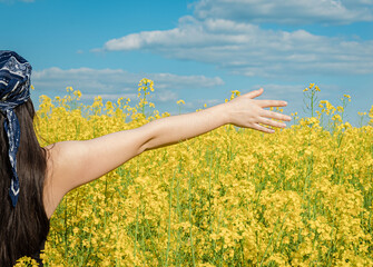 Girl with outstretched hand against the background of a blooming yellow field