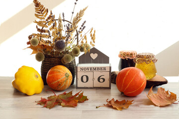 Calendar for November 6 : the name of the month in English, the numbers 0 and 6, a bouquet of dried flowers in a basket, pumpkins, maple leaves, jam jars on a gray table