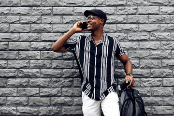 stylish african american man calling, talking on the phone, eating scooter, against black brick wall background