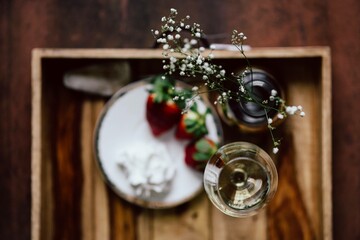 Strawberries with cream and glass of white wine on wooden tray