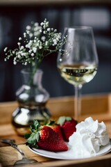 Strawberries with cream and glass of white wine on wooden tray