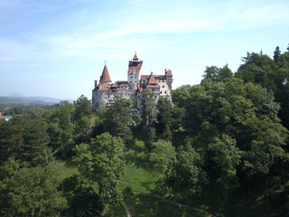 Fototapeta na wymiar Aerial view of Bran castle in Transylvania, Romania with white walls, red roofs, green trees and blue sky