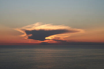 Red sunset over the sea. The setting sun hides behind a fluffy cloud and highlights it from the inside. Copy space.