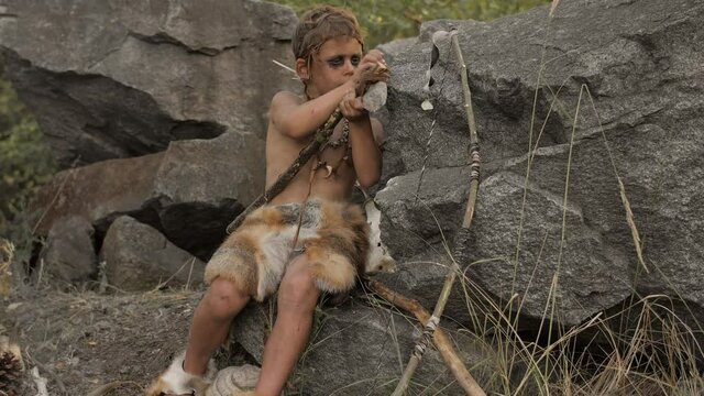 Caveman, manly boy making primitive stone weapon in camp