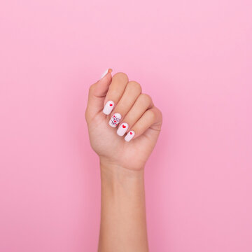 Beautiful female hand with creative manicure nails, hearts and Valentine's day design, on pink background