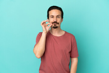 Young caucasian man isolated on blue background showing a sign of silence gesture