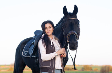 portrait of beautiful black horse  with his owner and rider  posing in green grass meadow. autumn...